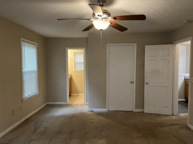 unfurnished bedroom with ceiling fan, ensuite bathroom, light colored carpet, and multiple windows