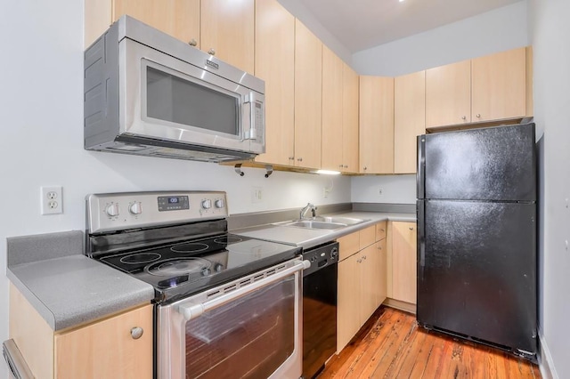 kitchen with black appliances, a sink, light brown cabinetry, light wood-style flooring, and light countertops