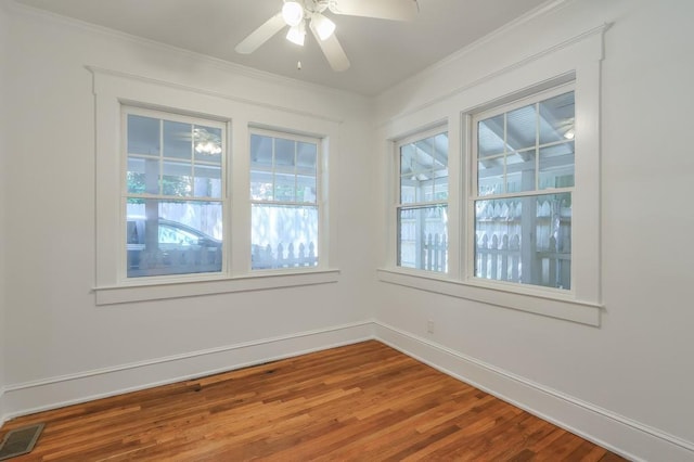 empty room with ceiling fan, wood finished floors, baseboards, and ornamental molding
