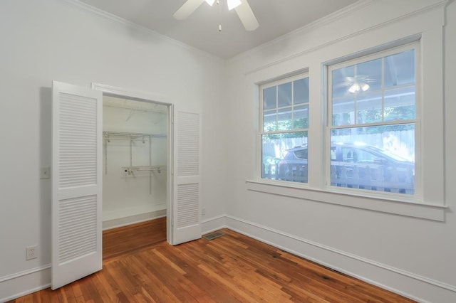 unfurnished bedroom with wood finished floors, ornamental molding, a closet, baseboards, and a ceiling fan