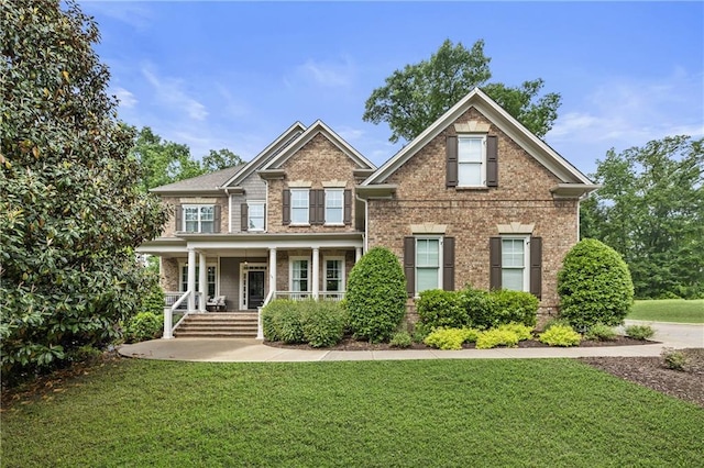 craftsman inspired home featuring brick siding, covered porch, and a front yard