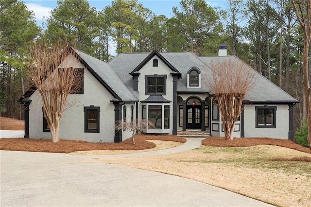 french country home featuring roof with shingles, french doors, a chimney, and stucco siding