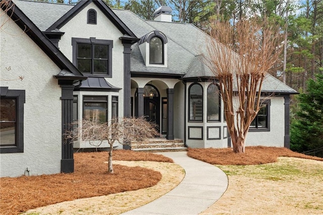 french provincial home with roof with shingles, a chimney, and stucco siding