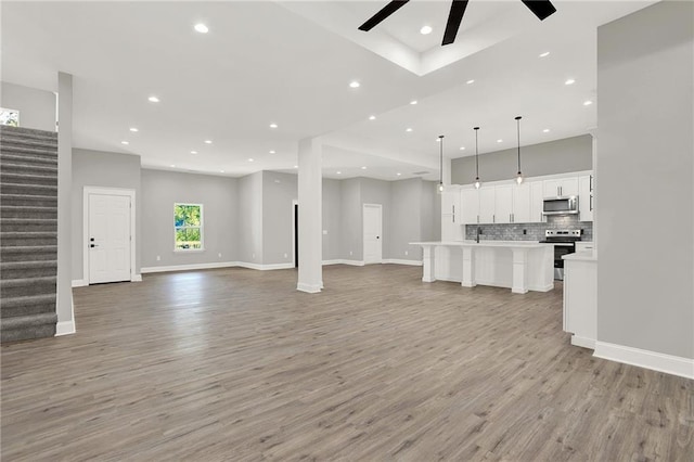 unfurnished living room with stairs, recessed lighting, light wood-type flooring, and ceiling fan