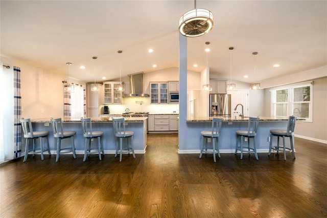 kitchen with wall chimney exhaust hood, pendant lighting, appliances with stainless steel finishes, and a kitchen breakfast bar