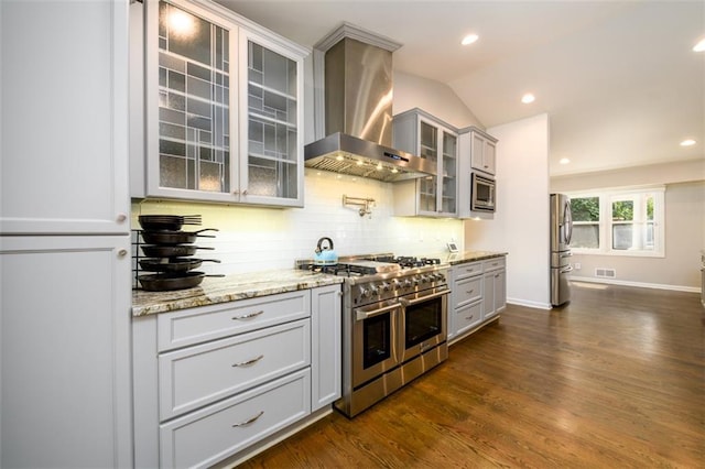 kitchen with appliances with stainless steel finishes, lofted ceiling, dark hardwood / wood-style floors, wall chimney exhaust hood, and decorative backsplash