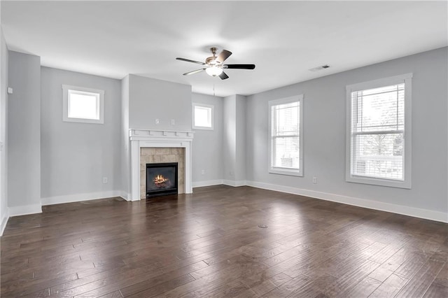 unfurnished living room with a tile fireplace, baseboards, ceiling fan, and dark wood-style floors