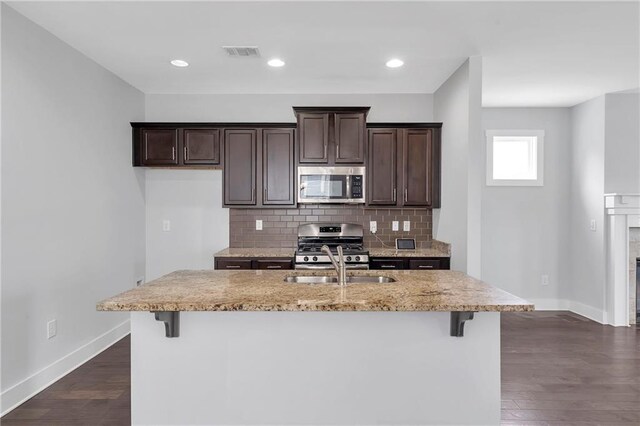 kitchen featuring appliances with stainless steel finishes, baseboards, dark brown cabinetry, decorative backsplash, and a breakfast bar