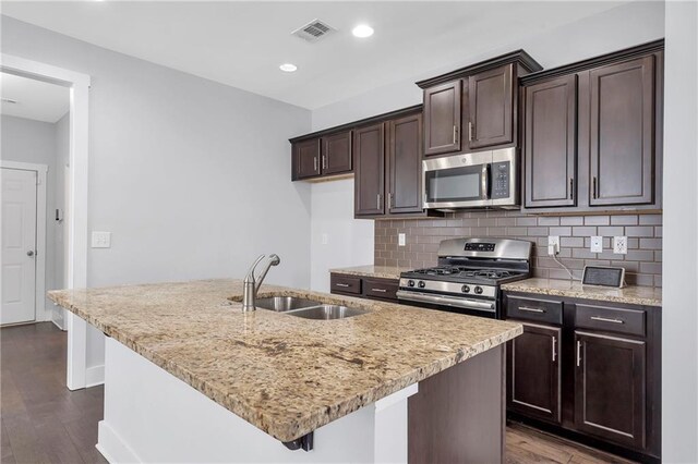 kitchen with appliances with stainless steel finishes, a sink, dark wood finished floors, backsplash, and dark brown cabinets
