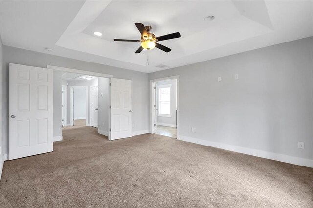 unfurnished bedroom featuring carpet flooring, a tray ceiling, baseboards, recessed lighting, and ceiling fan