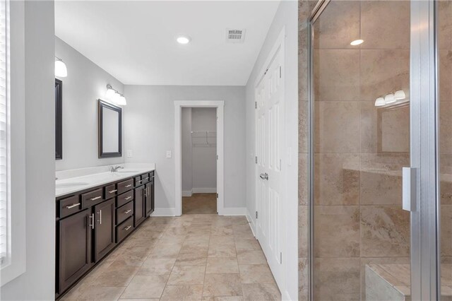 bathroom with a stall shower, double vanity, a spacious closet, and baseboards