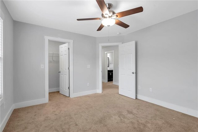 unfurnished bedroom featuring carpet floors, a spacious closet, baseboards, ceiling fan, and a closet