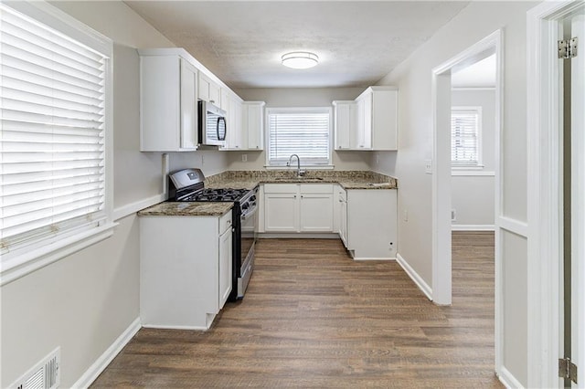 kitchen featuring visible vents, stainless steel microwave, gas range oven, white cabinetry, and a sink