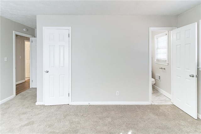 unfurnished bedroom with visible vents, light colored carpet, ensuite bath, and baseboards