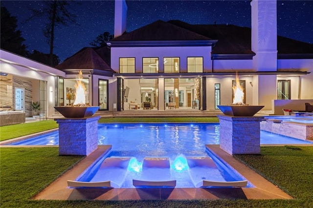 back of house at night with a yard, an outdoor pool, and an in ground hot tub