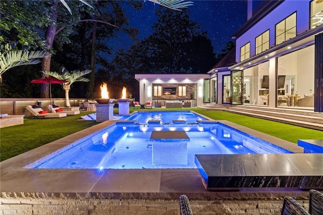 pool at night featuring a pool with connected hot tub and an outdoor hangout area