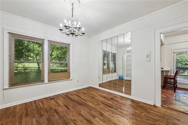 empty room featuring a chandelier, hardwood / wood-style floors, crown molding, and baseboards