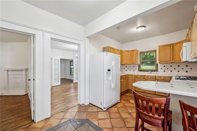 kitchen with white appliances, tile counters, decorative backsplash, and light wood-type flooring