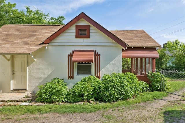 view of front of property featuring roof with shingles, fence, and stucco siding