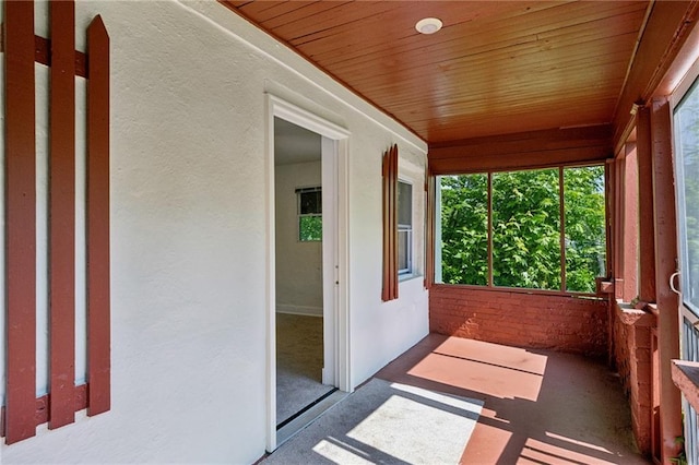 unfurnished sunroom with wood ceiling, a textured wall, and carpet flooring