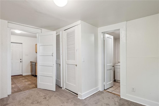unfurnished bedroom featuring light colored carpet, a closet, ensuite bath, and baseboards