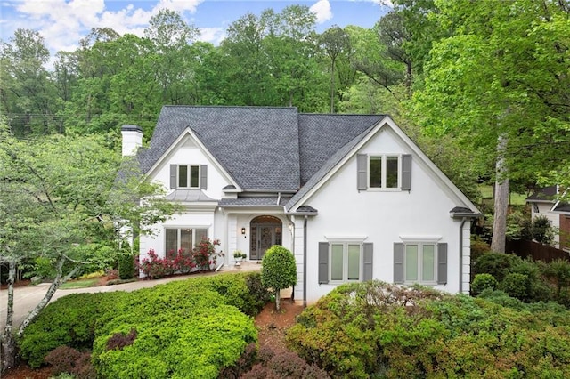 view of front of house with stucco siding, a chimney, and a shingled roof