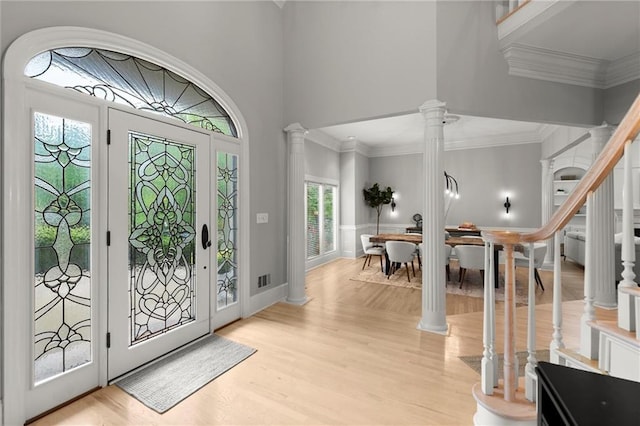entryway with crown molding, a towering ceiling, decorative columns, and wood finished floors