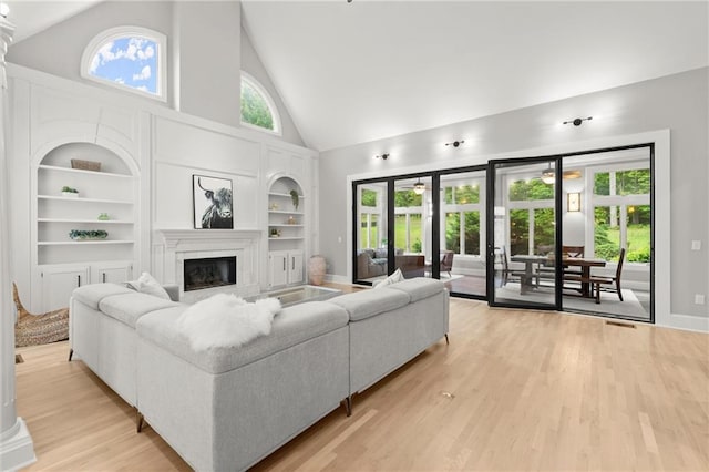 living room featuring baseboards, light wood finished floors, built in features, a fireplace, and high vaulted ceiling