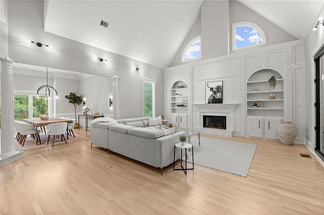 living area featuring visible vents, high vaulted ceiling, built in features, and decorative columns