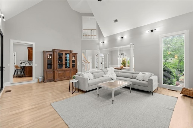 living room featuring stairway, visible vents, light wood-type flooring, and high vaulted ceiling