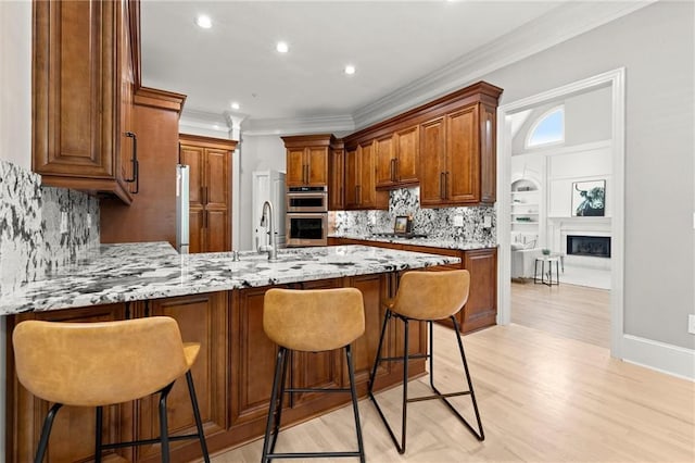 kitchen with double oven, light stone counters, light wood-style flooring, a sink, and a peninsula