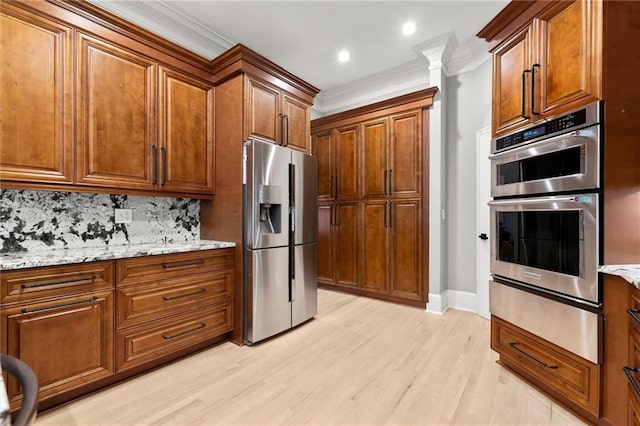kitchen featuring crown molding, appliances with stainless steel finishes, light wood finished floors, a warming drawer, and brown cabinetry