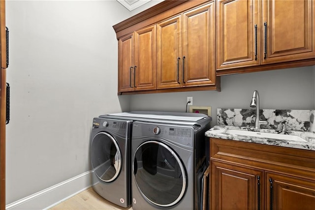 washroom featuring a sink, washing machine and dryer, baseboards, light wood finished floors, and cabinet space