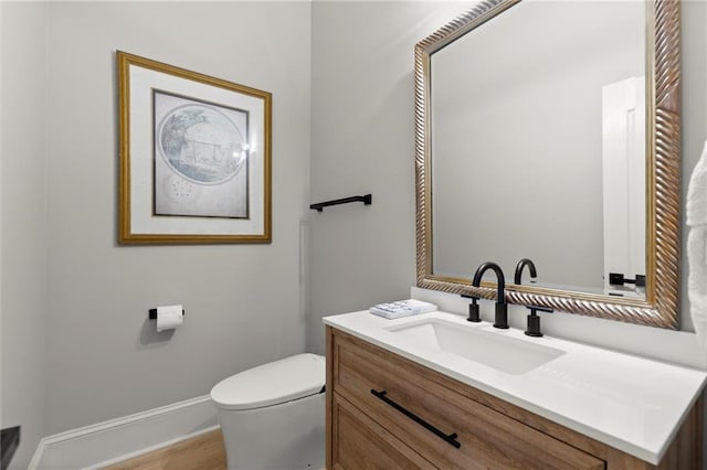 bathroom with baseboards, wood finished floors, toilet, and vanity