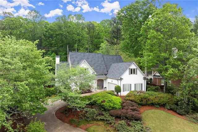view of front of home with stucco siding, a chimney, and a view of trees