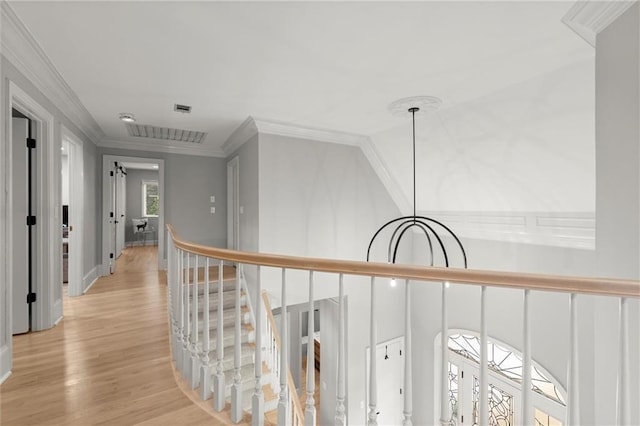 corridor with crown molding, an upstairs landing, a chandelier, and light wood-type flooring