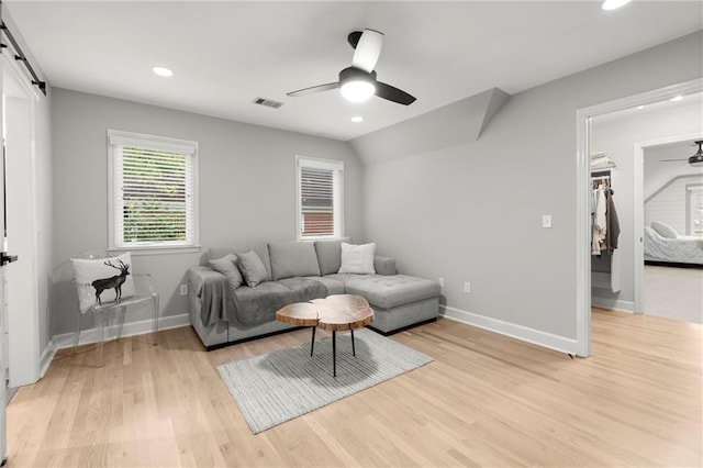 living area featuring light wood-style flooring, a barn door, ceiling fan, baseboards, and visible vents