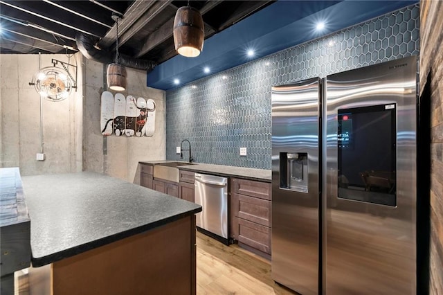 kitchen with light wood-style flooring, a sink, appliances with stainless steel finishes, dark countertops, and a peninsula