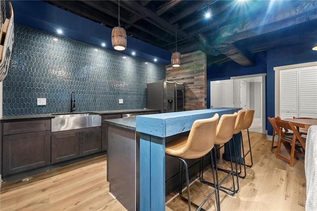 kitchen with a sink, light wood-style floors, a center island, a breakfast bar, and stainless steel fridge with ice dispenser