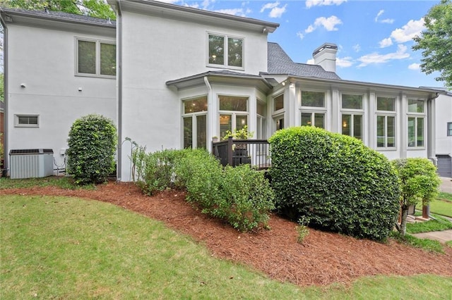 back of property featuring a chimney, central AC unit, a yard, and stucco siding