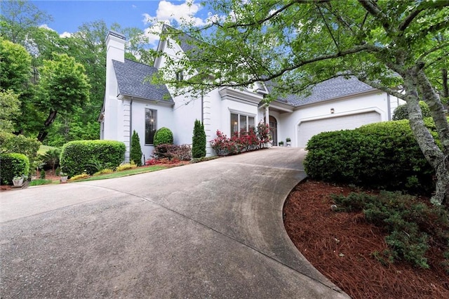 view of front of house featuring a chimney, stucco siding, roof with shingles, concrete driveway, and an attached garage