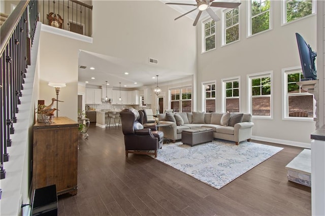living room featuring stairway, ceiling fan, dark wood finished floors, and a towering ceiling