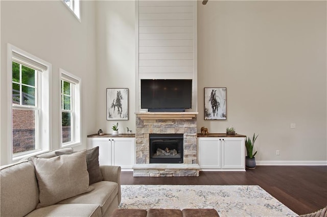 living area with baseboards, a high ceiling, a fireplace, and dark wood finished floors