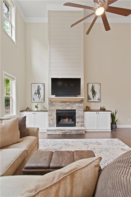 living room featuring crown molding, a high ceiling, a fireplace, and ceiling fan