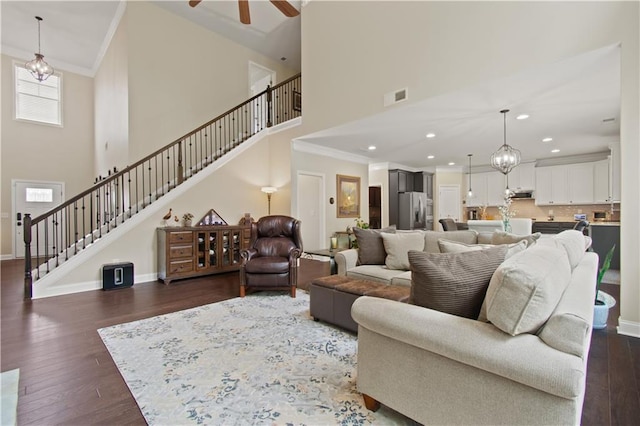 living area featuring visible vents, crown molding, a towering ceiling, and stairway