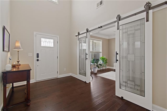 foyer with visible vents, a barn door, dark wood finished floors, and baseboards