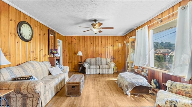 living room featuring light wood-type flooring, ceiling fan, ornamental molding, wood walls, and a textured ceiling