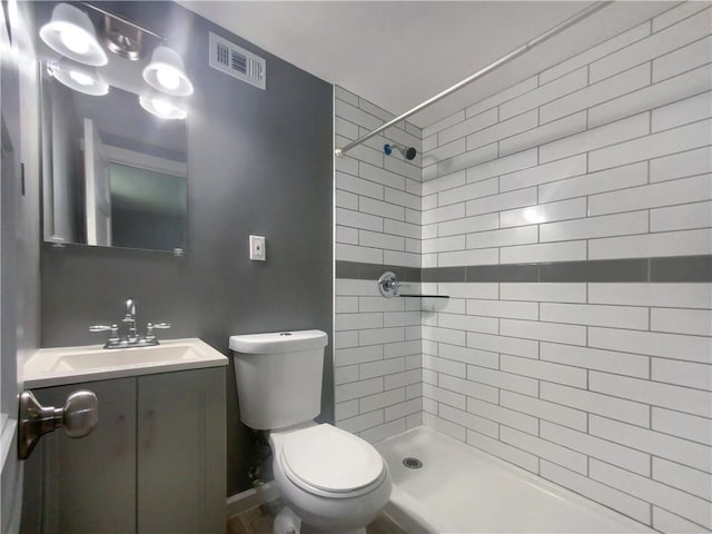 bathroom featuring a tile shower, vanity, and toilet