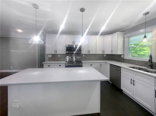 kitchen featuring appliances with stainless steel finishes, sink, decorative light fixtures, white cabinets, and a center island