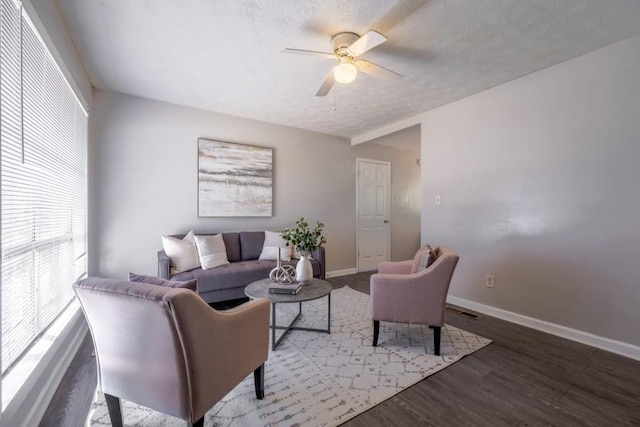 living area with visible vents, a ceiling fan, a textured ceiling, wood finished floors, and baseboards